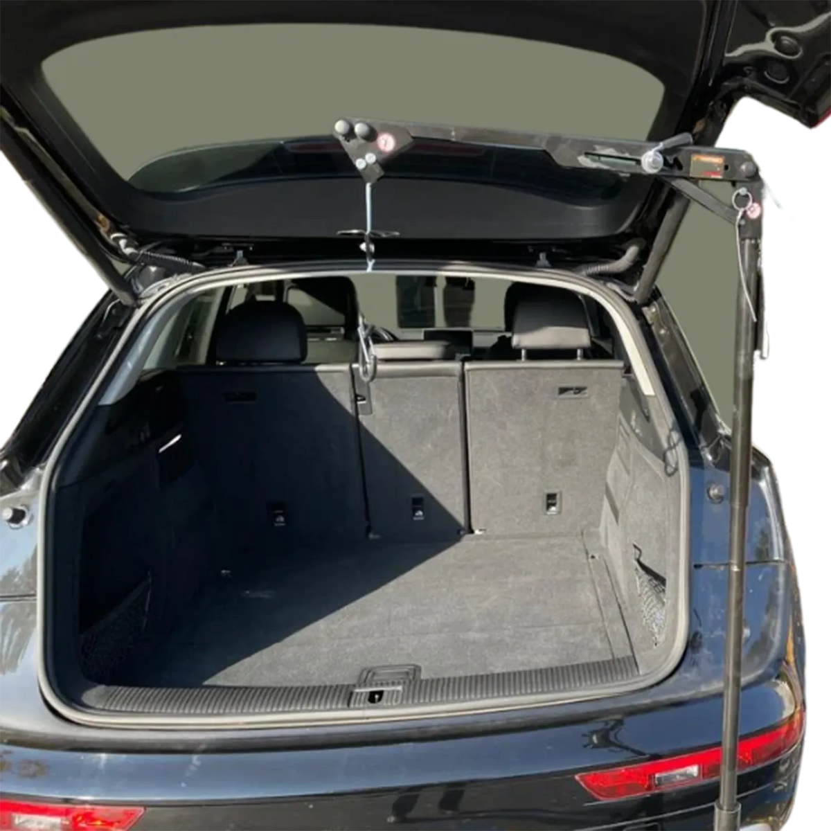 A black metal car trunk support stand with hydraulic arms is shown holding up an open trunk of a dark gray SUV against a white background.