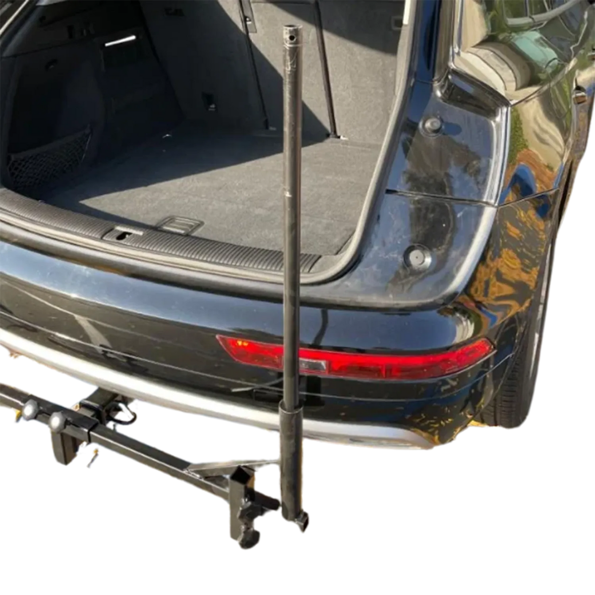 A black metal hitch-mounted cargo carrier rack attached to the rear hitch of a dark car, with the open trunk visible behind it on a white background.