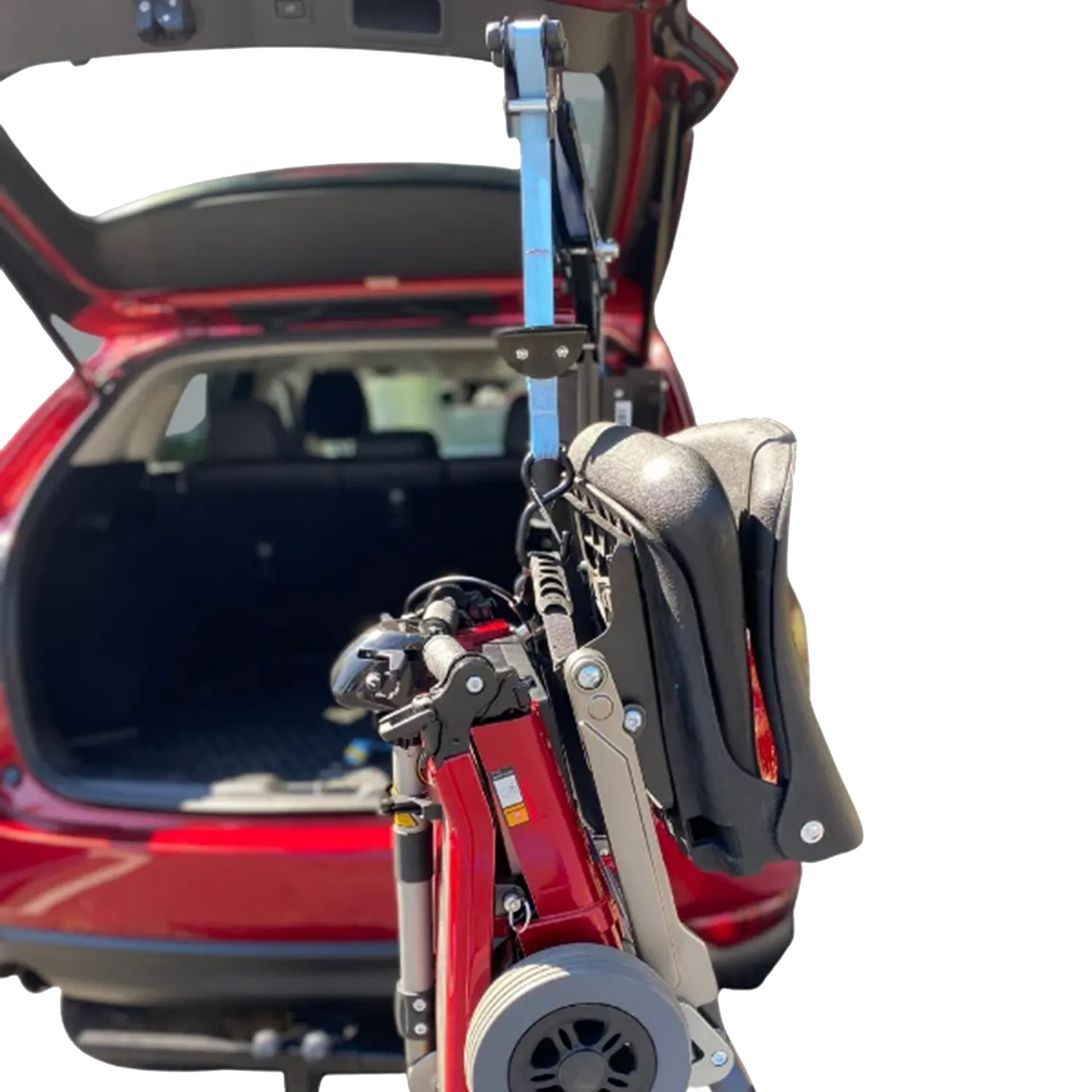 A red and black electric folding wheelchair mounted on a hitch-style carrier rack attached to the open trunk of a red car, shown against a white background.